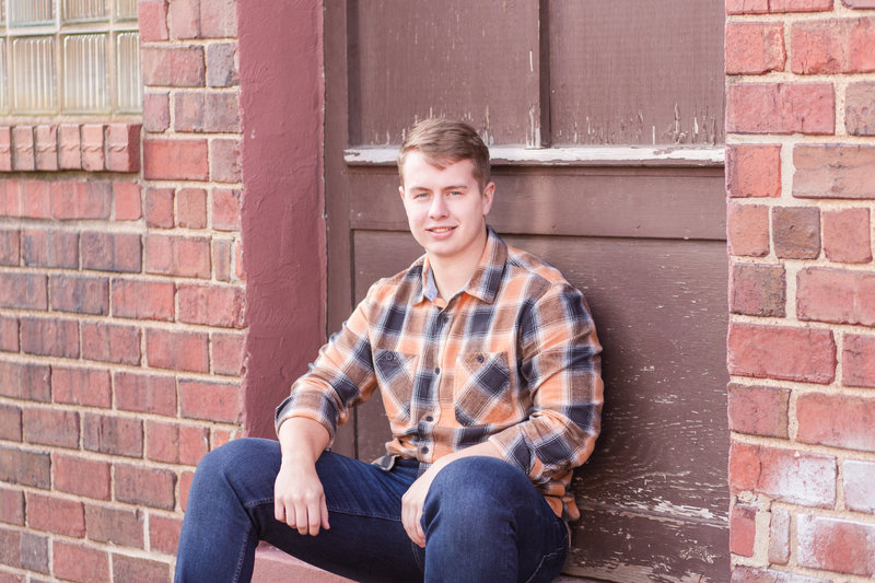 dalton senior guy sitting in front of brick wall, photographed downtown Wooster ohio photographed by Jamie Lynette Photography canton ohio senior photographer