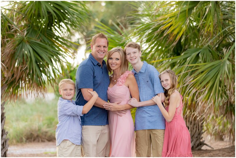 Close up picture of a family smiling for a photo in front of palm trees.
