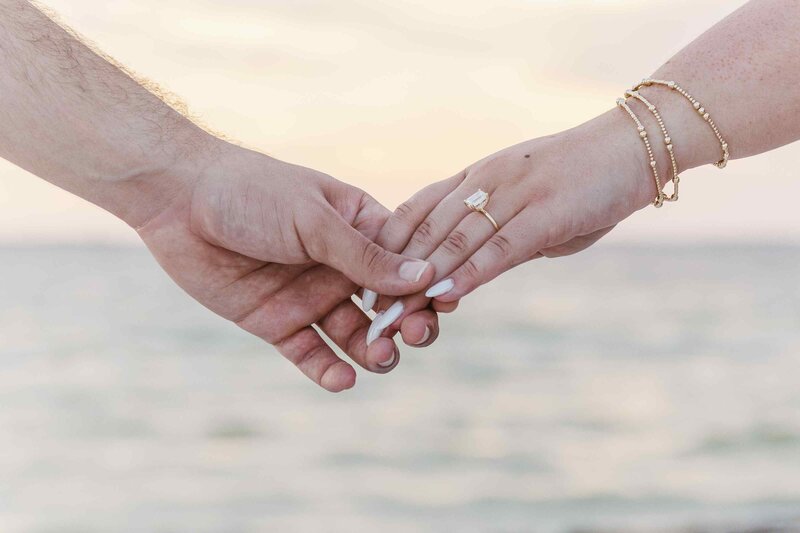 Couple holds hands with the ocean sunset in the background