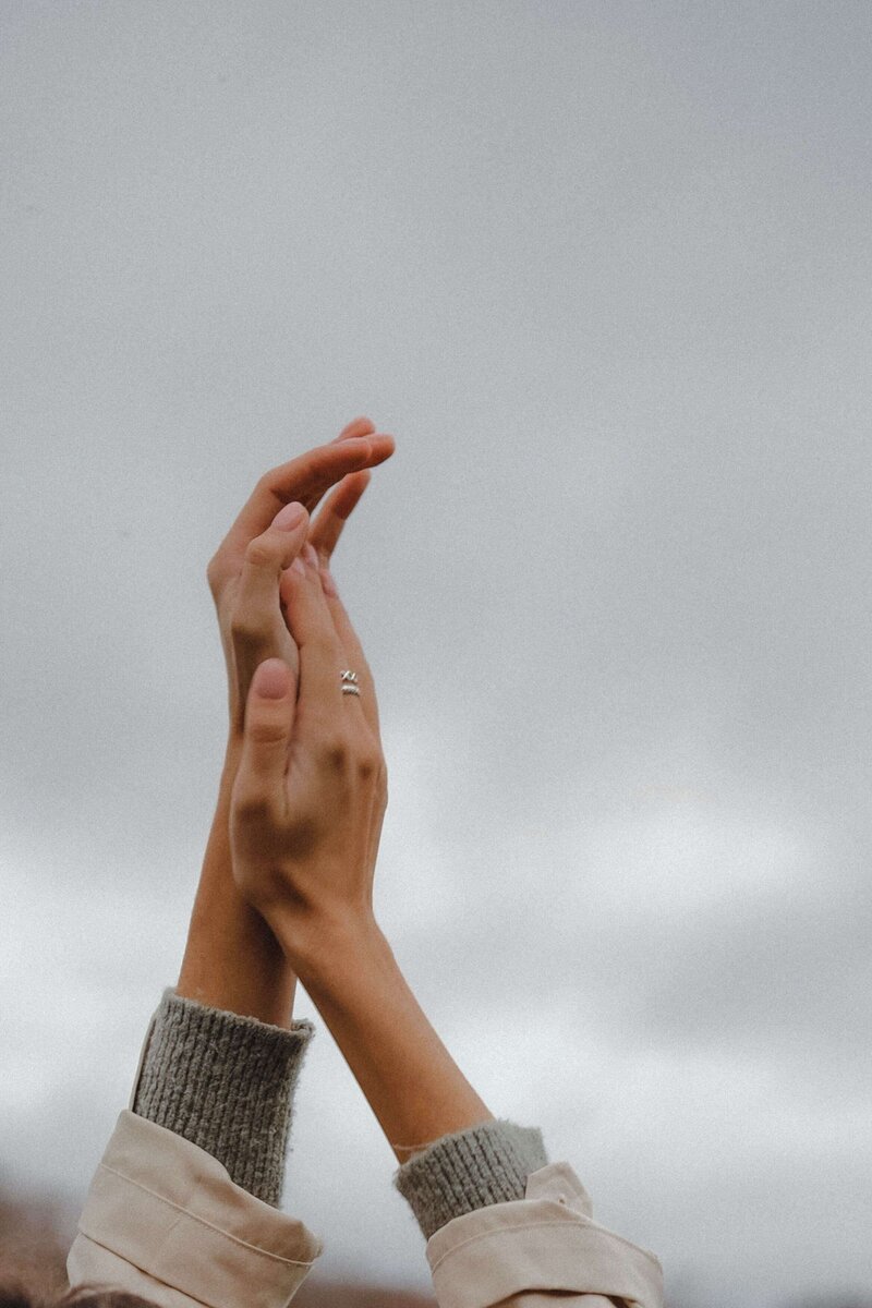Frauenhände, wie in einem Gebet zum Himmel voller Dankbarkeit und Befreiung gerichtet, im Hintergrund verschwommen die Gischt: Eine Geste der inneren Ruhe, des Dankes und der Erlösung