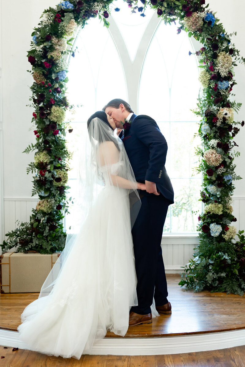 bride and groom sealed a kiss under the floral arch at dallas wedding, by bella vista wedding planning