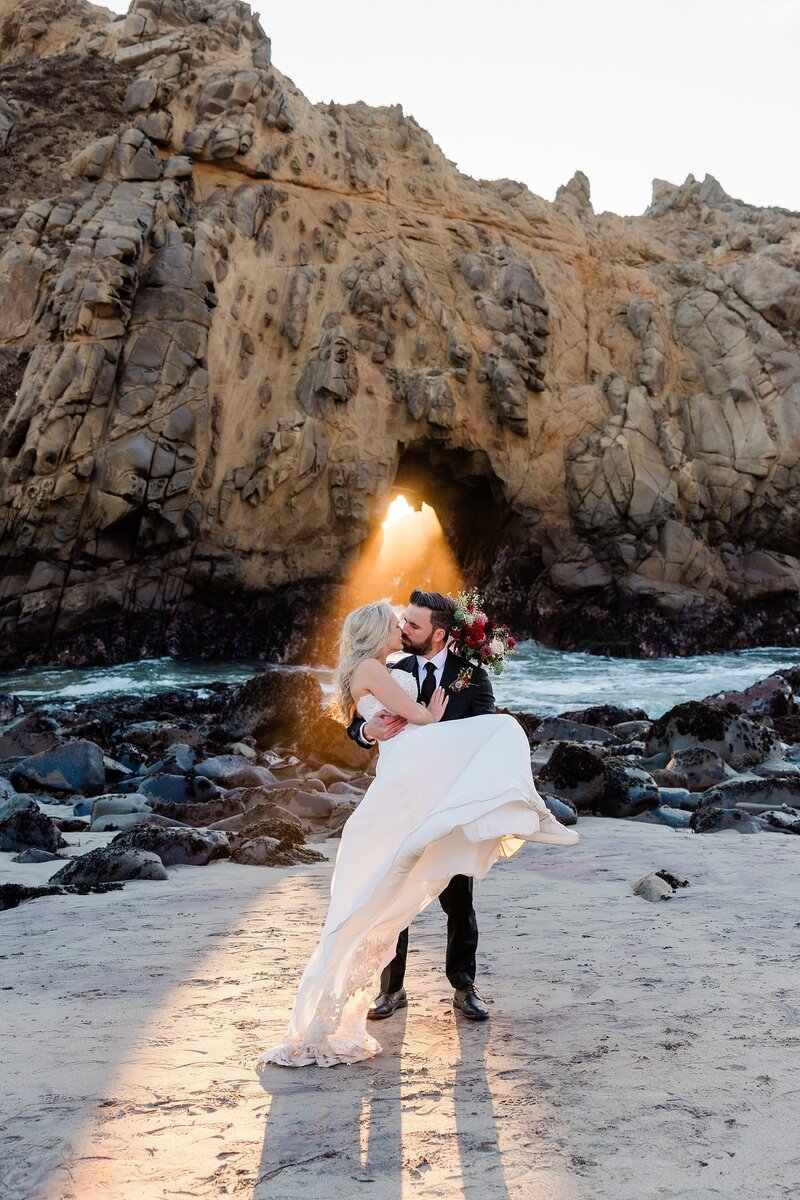 A bride and groom kiss with the sun ray shining through the keyhole at Pheiffer Beach.