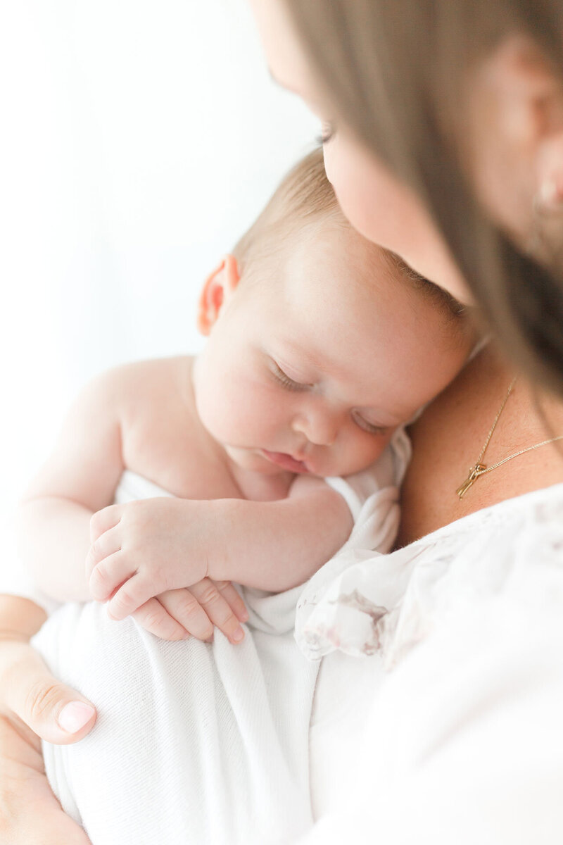 In Nahaufnahe wie die Mama das schlafende Baby im Arm hält entsteht ein Babyfoto als Portrait.