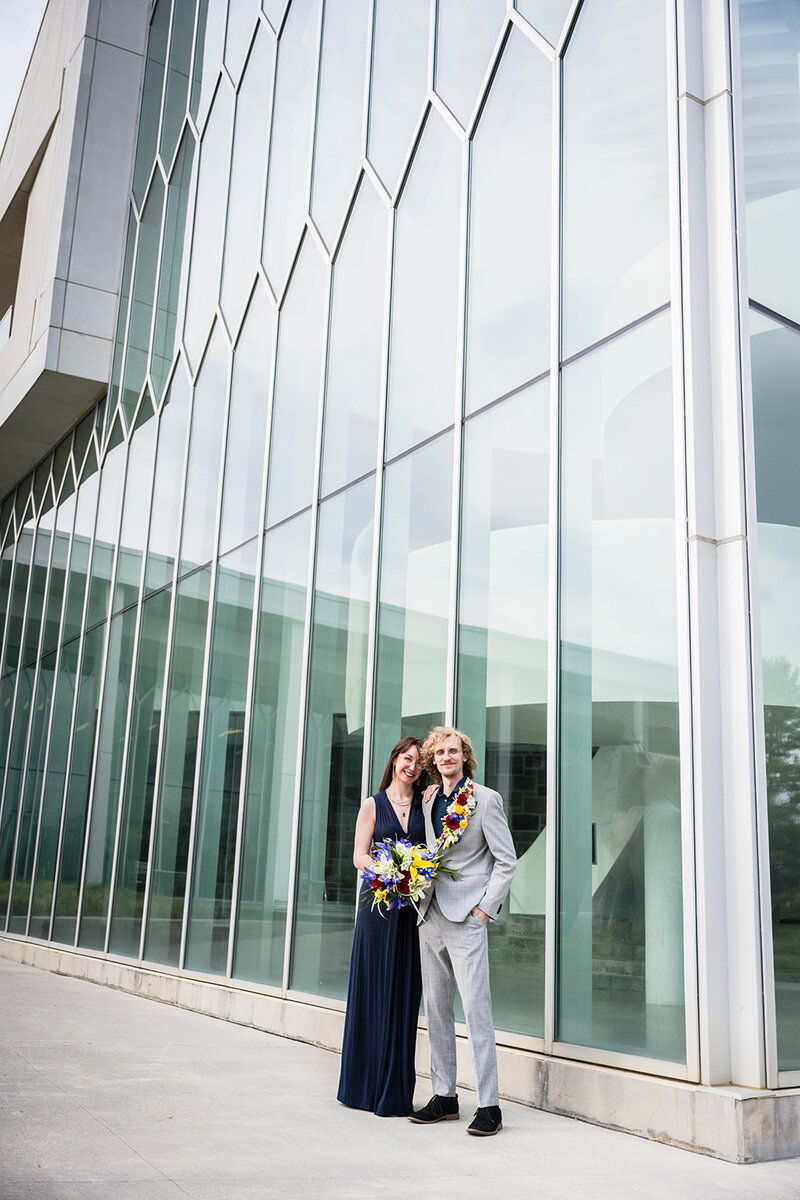 A couple on their elopement day stand outside the Virginia Tech Moss Arts Center and pose together for a photo.