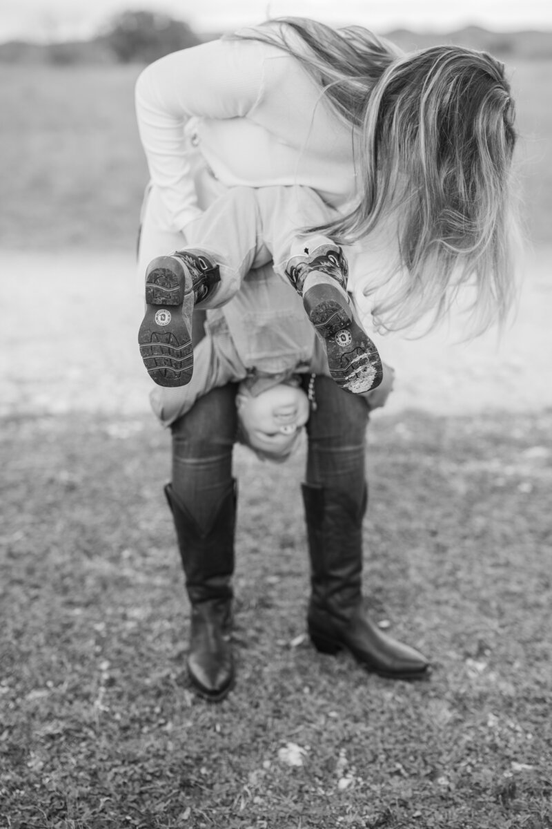 Black and white image of a mom carrying her smiling son upside down