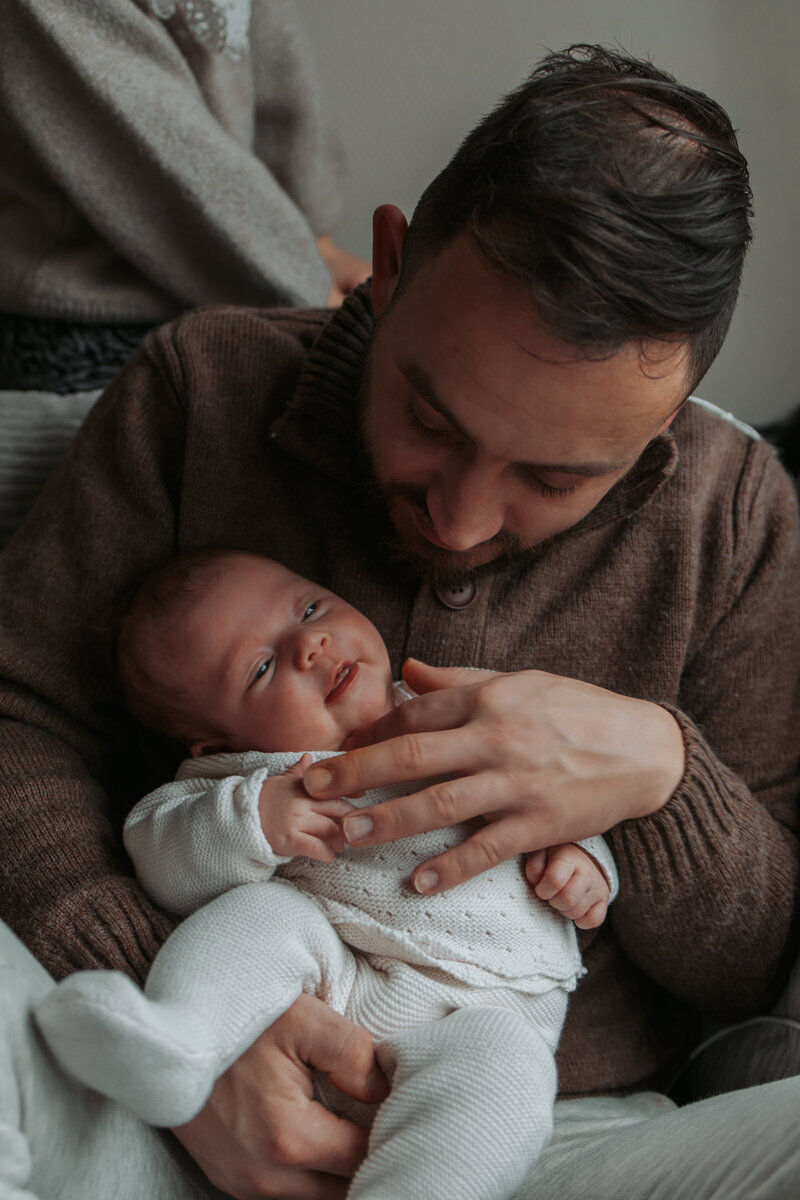 Een vader houdt zijn baby liefdevol vast, met een warme glimlach op zijn gezicht.