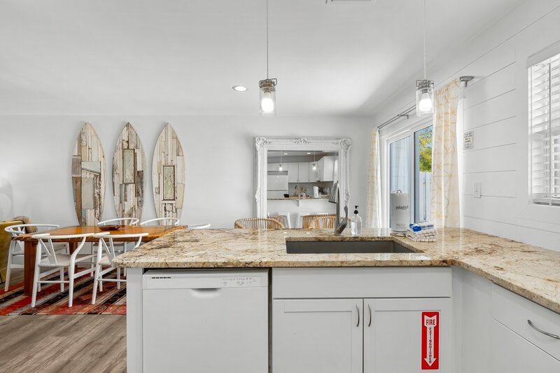 View from kitchen to dining area featuring reclaimed wood surfboard wall art and large mirror reflecting bright natural light.