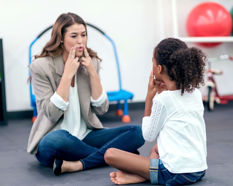 Speech-language pathologist working with a school aged child on prompt mouth exercises in a bright therapy room in Somerset, NJ.