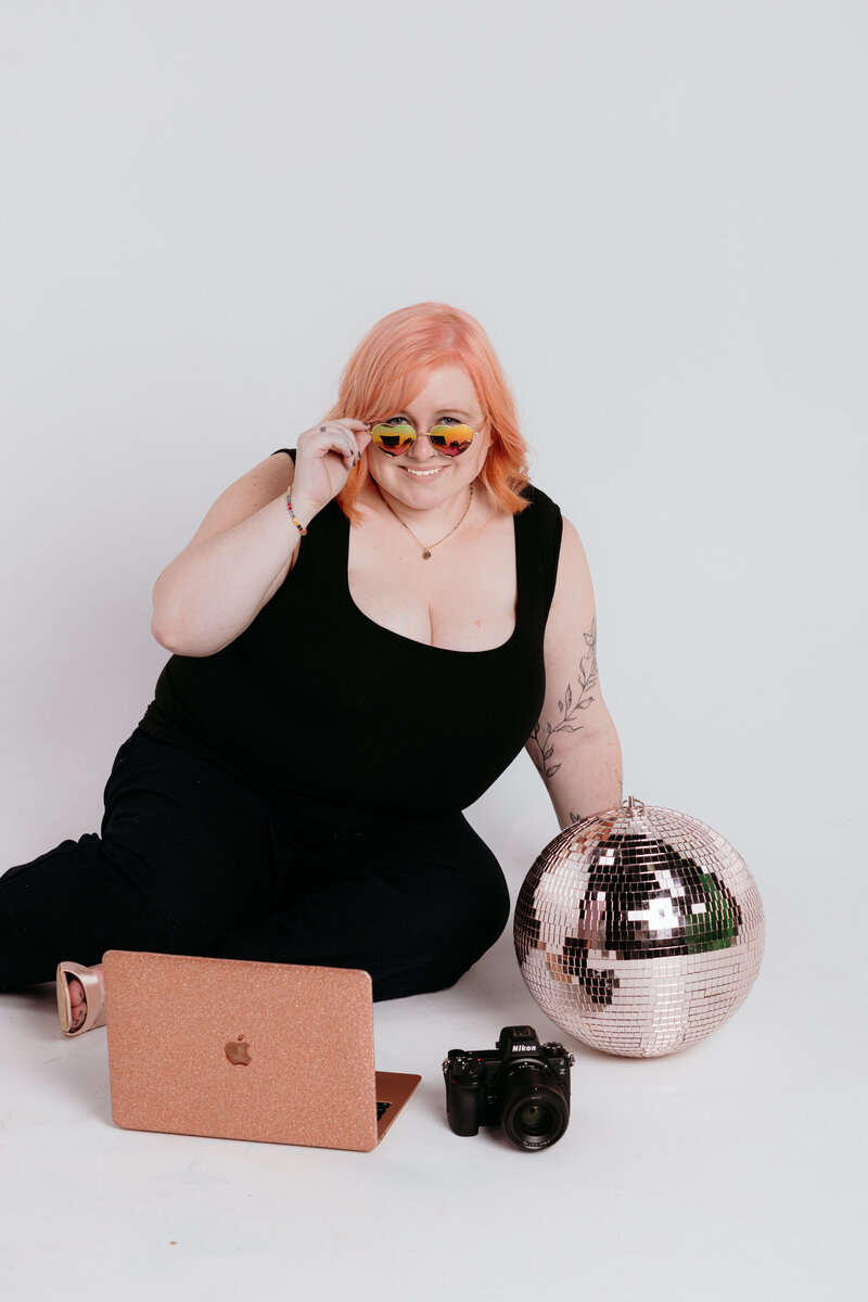 Melissa Cook, a Northern VA and Leesburg Wedding Photographer, Posed with sunglasses, a camera, laptop and disco ball