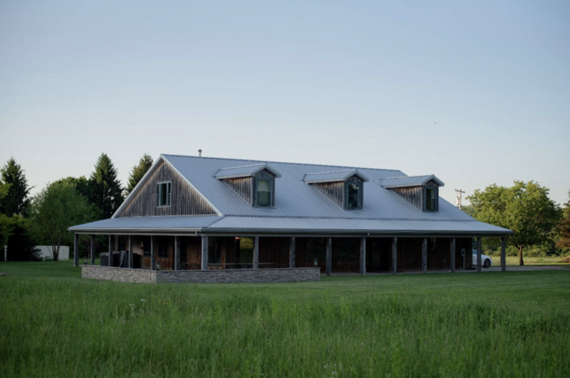 Rustic lodge-style building with a wraparound porch and metal roof, set on open green fields at Bear Ridge Destination.

