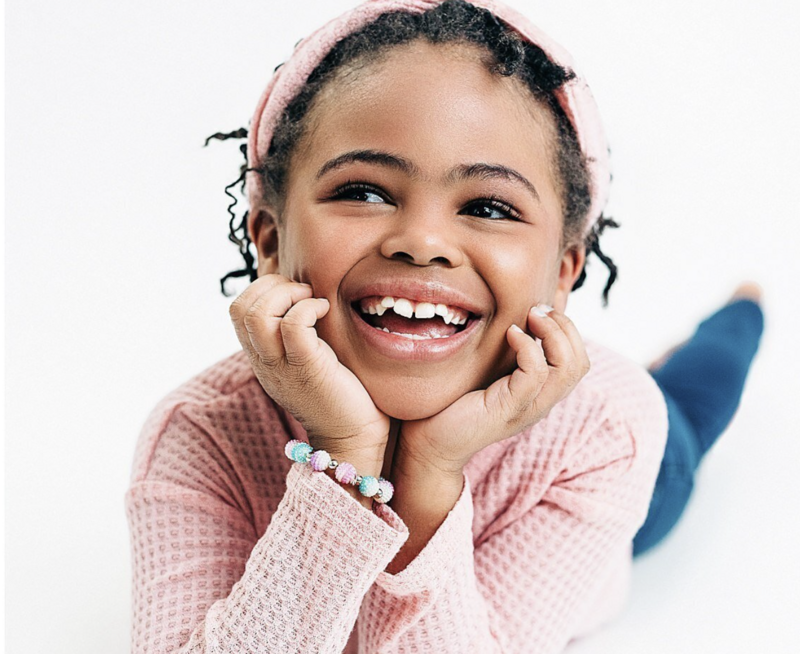 Smiling young boy sitting on a white backdrop with no shoes.