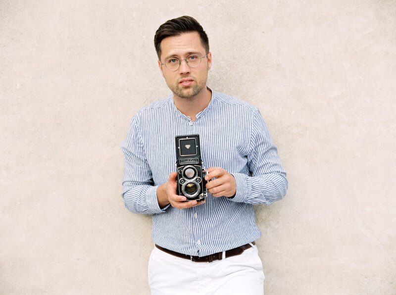 Photographer, Ezechiel Theler, stands with his film camera in a blue and white striped shirt