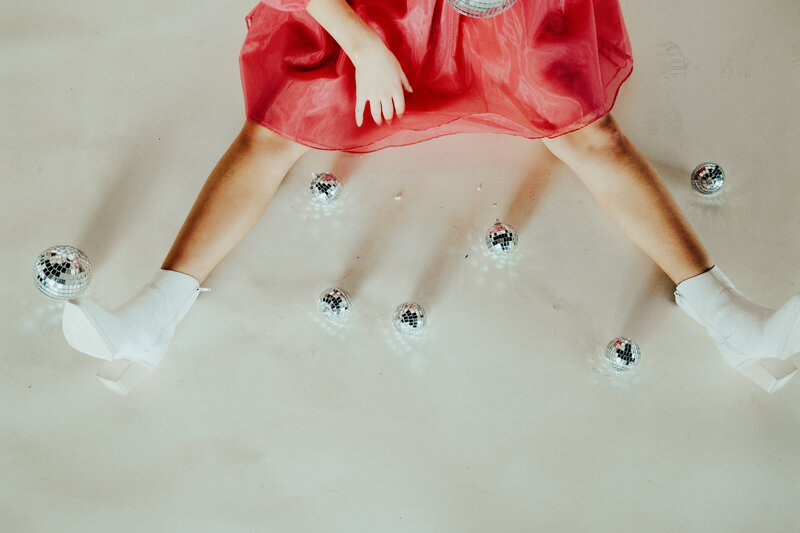 girl in a pink dress sitting on the floor surrounded by small mirror balls