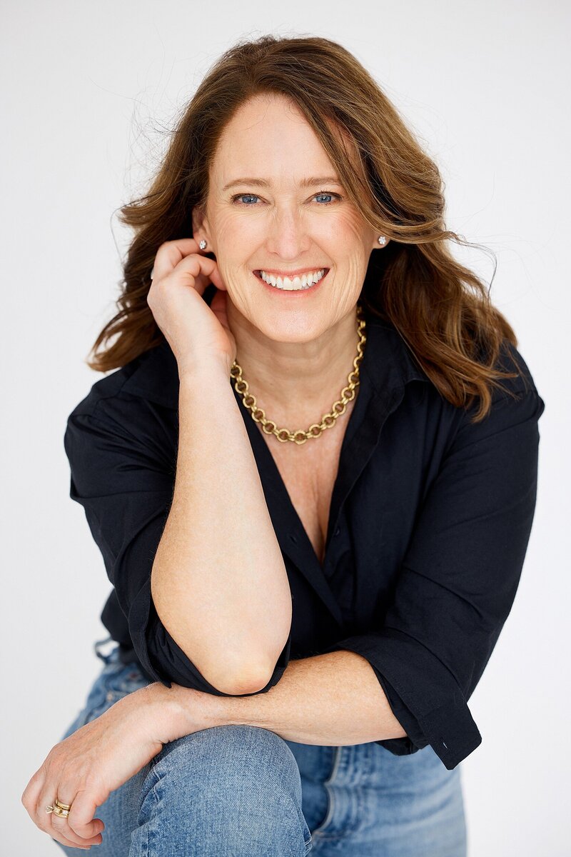 Smiling woman in black blouse and jeans posing confidently for personal branding headshot on white background