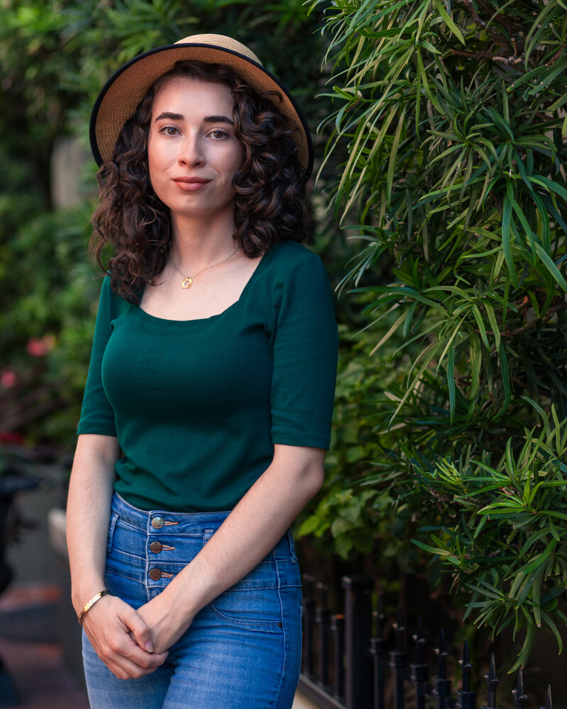 Girl smiling in jeans, a green shirt, and a sun hat