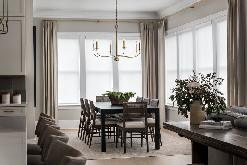 Modern dining room in Lake Norman, NC, with a sleek black table, gold chandelier, and neutral decor.