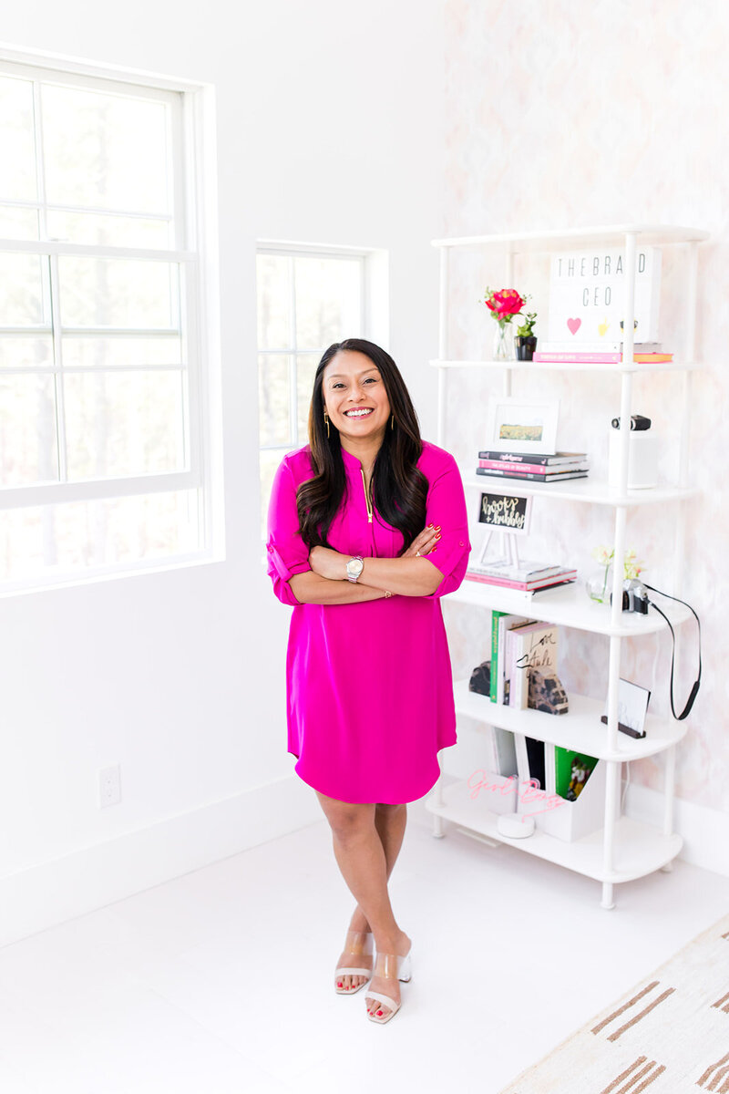 Mallika Malhotra confidently standing with arms crossed in a bright office, promoting her workshop on mastering personal branding.