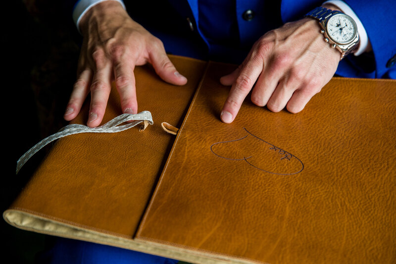 Close-up of a groom pointing to the personalized lettering on a luxurious leather wedding album cover.