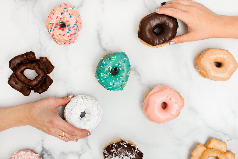 Two hands grabbing assorted donuts on white background - Daylight Donuts
