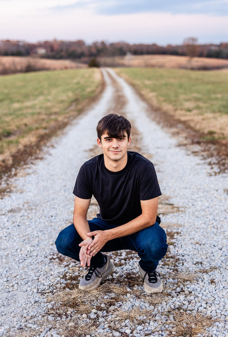 Senior guy sitting in a gravel road with a scenic view behind him. 
