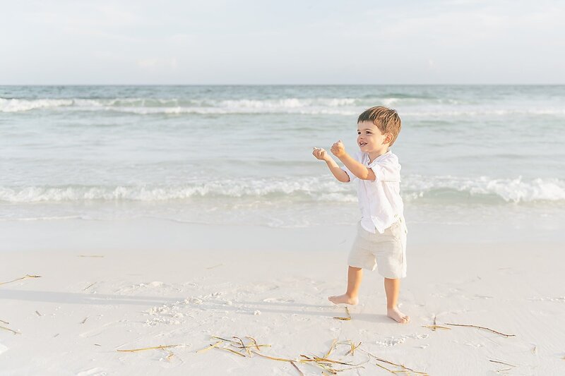 a little boy enjoying the sand on the beach in front of the water