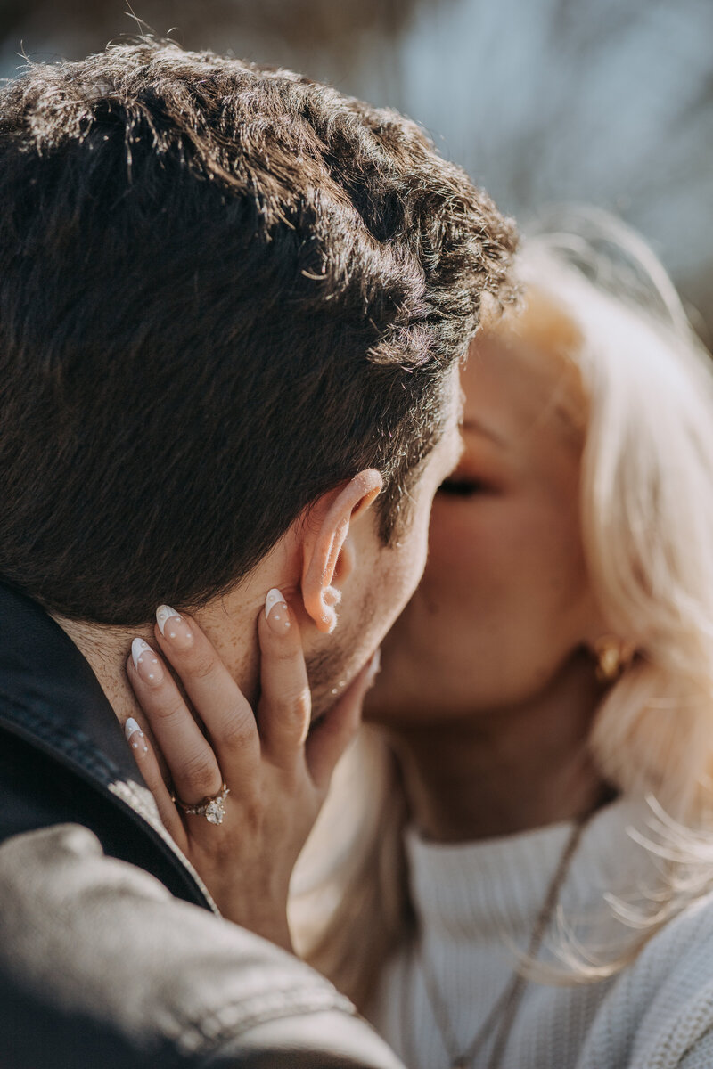 Close-up of engagement ring on woman’s finger as she holds fiancé’s face while kissing at Lamar Park, Oxford.