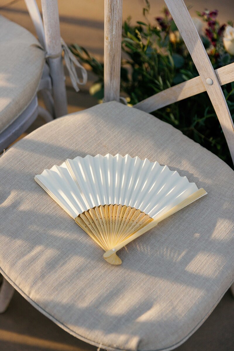 Handheld paper fan sitting on chair at a wedding ceremony.