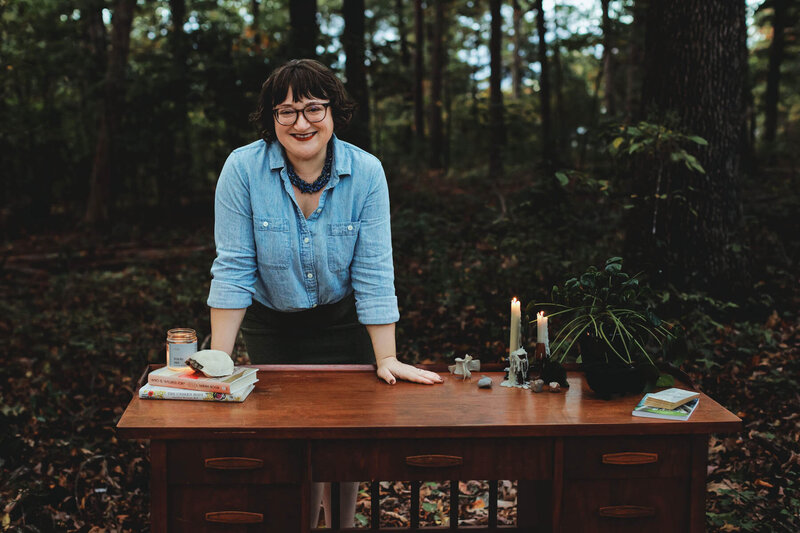 Energy worker Ash Stinson smiles while leaning over a wooden desk set in the forest