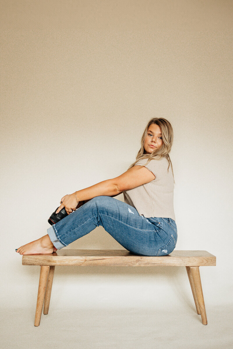 Portrait of Taylor Ragusett, a Charleston photographer sitting casually on a wooden bench with a camera in hand.