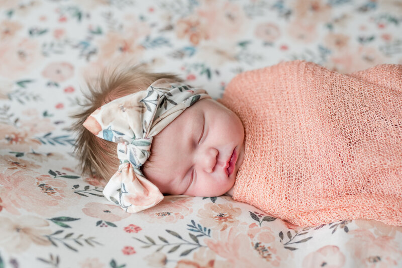 Sleeping baby with bow wrapped in orange blanket