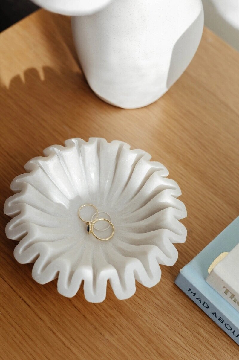 Close-up shot of a white marble fluted dish on a wooden surface, holding three rings.