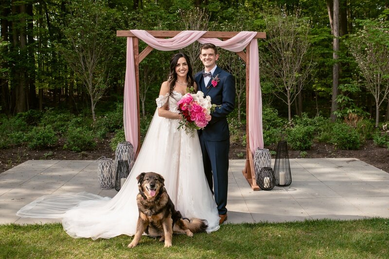 bride and groom smiling with their dog in front of them