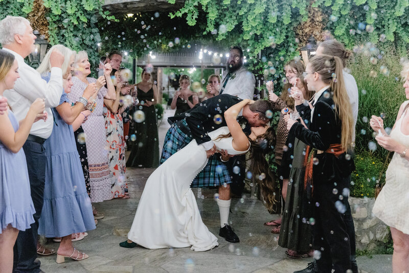 A groom dips his bride and kisses her while the guests blow bubbles