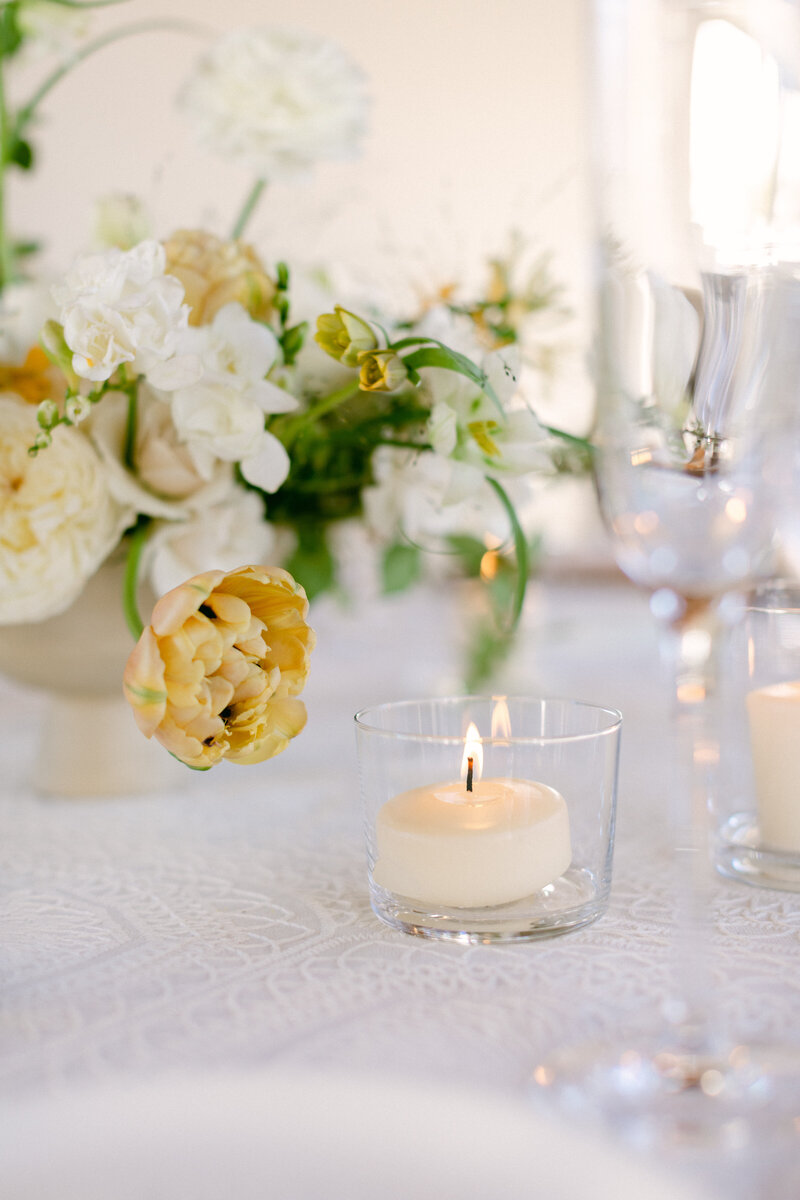 Tablescape photo showing a white lace tablecloth, a stunning textural floral centerpiece with a peach tulip and a candle