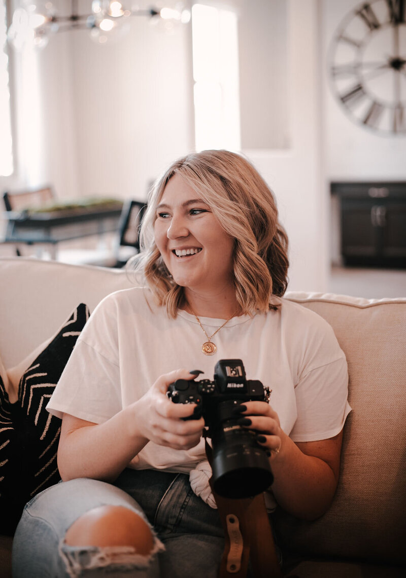 Fun and authentic candid photo of brand photographer sitting on a rock, laughing and holding a camera

