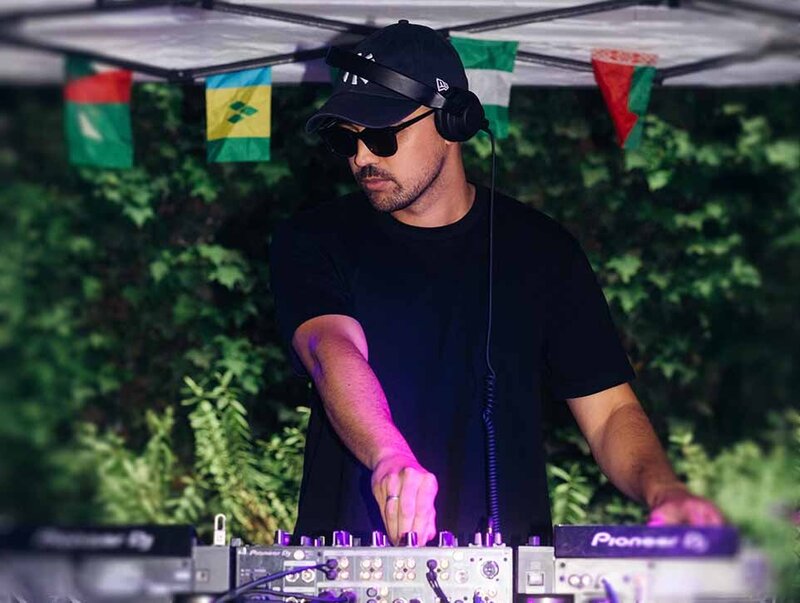 Male DJ mixing on DJ decks at a Party event, under a tent, with world flags