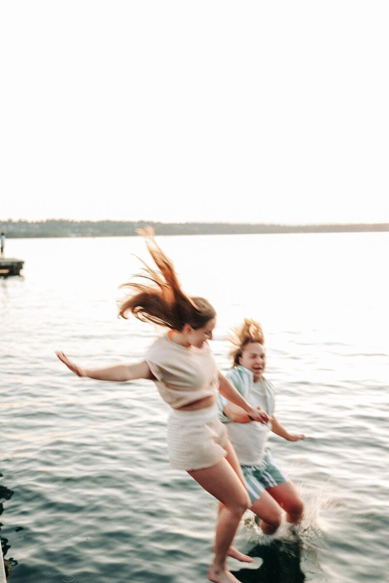 a couple hold hands as they jump off the dock into the water.