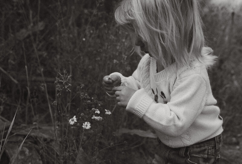 A husband and wife hold their baby and watch their dog play in the nearby lake.