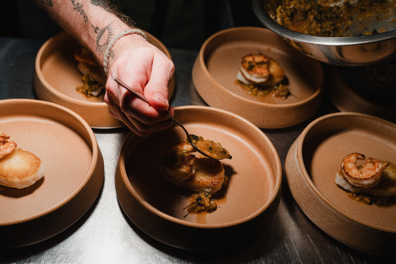 Chef adds garnish to seared scallops and prawns in uniform ceramic bowls at Sael Birmingham.