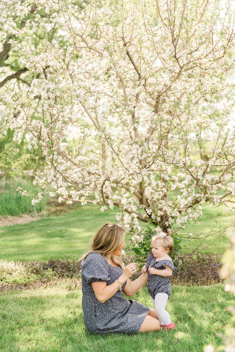 a mother sits in the grass with her toddler playing together