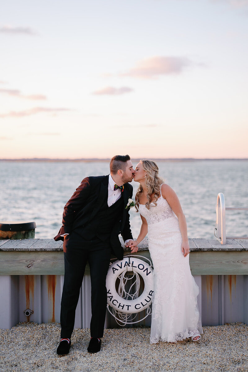 Couple kisses during sunset portraits on the bay at their Avalon Yacht Club wedding