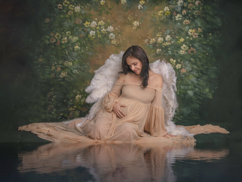 "Pregnant mom-to-be sitting gracefully on a fine art backdrop, with a serene water reflection, captured in an elegant and timeless maternity photography session in Ottawa."