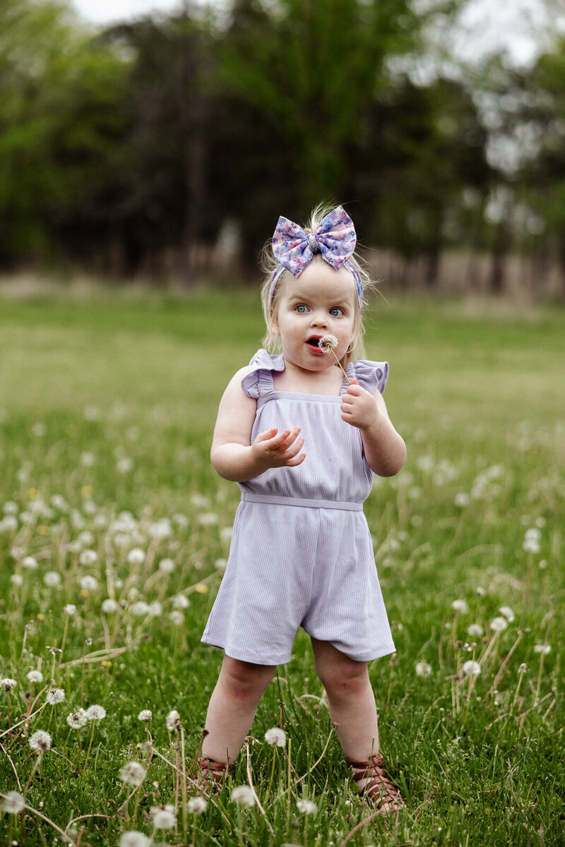 Toddler girl blowing on bubbles while standing in the grass. 