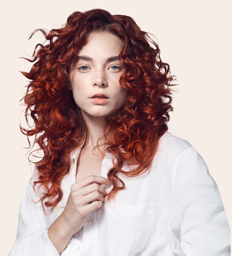Vibrant copper-red curly hair styled in voluminous layers, showcasing premium salon hair color and expert styling at Blake & Kwan Hairdressing in Sutherland Shire.