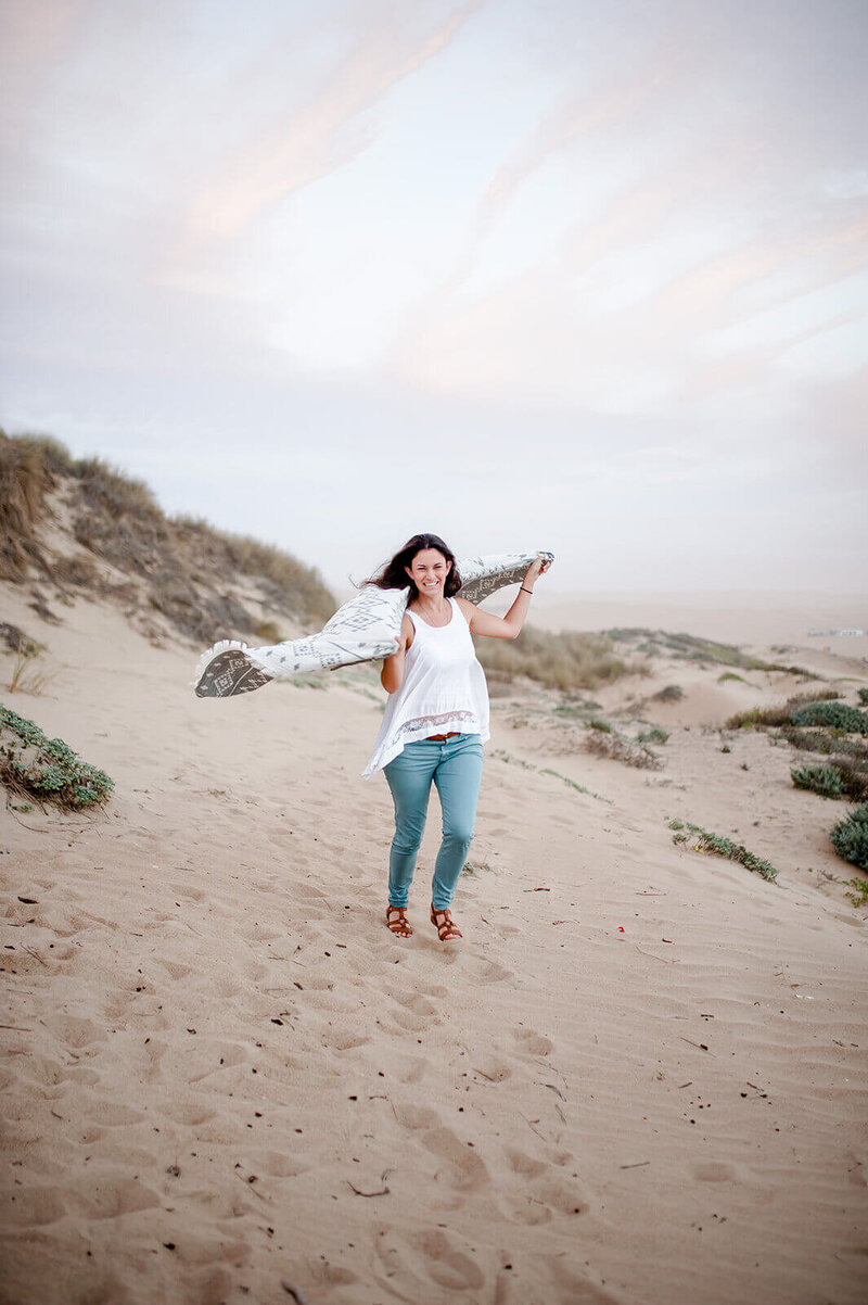 woman running down a sand dune holding a blanket