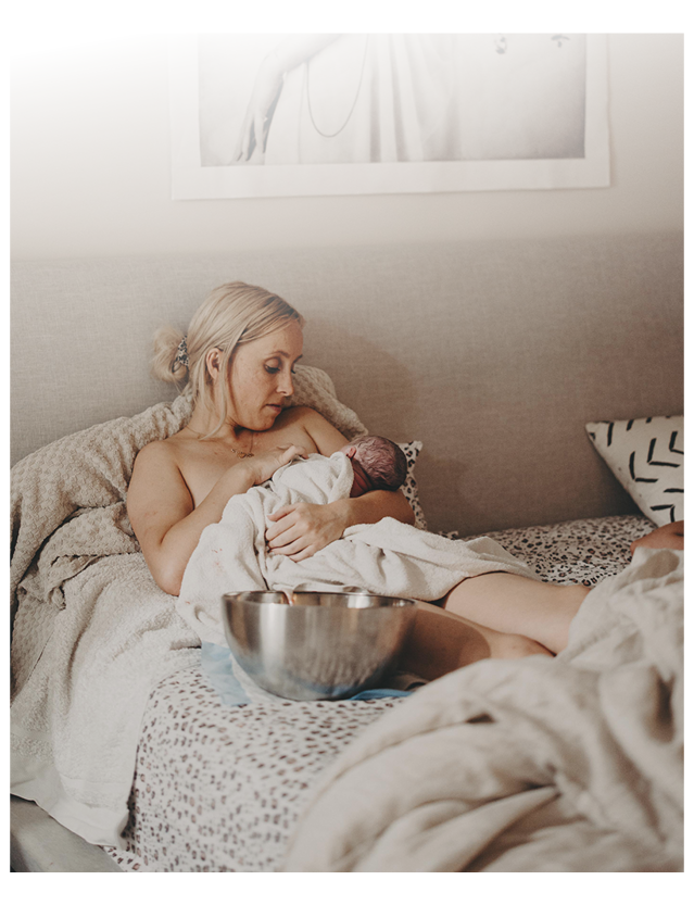 A mother sitting on her bed taking in the afterglow of the birth of her baby.