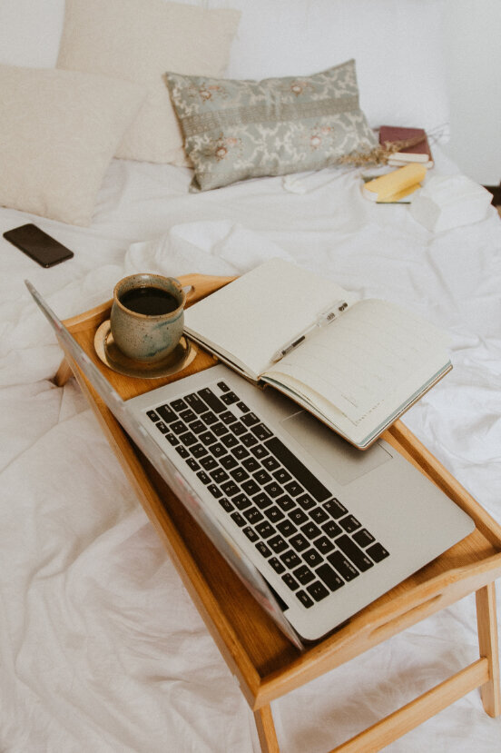 laptop, coffee mug, and notebook sitting on a bed