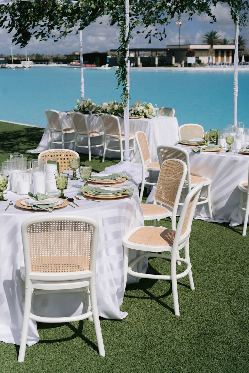 Long wood tables with pastel florals and Louis chairs beneath a suspended floral runner and crystal chandeliers in a Houston ballroom.