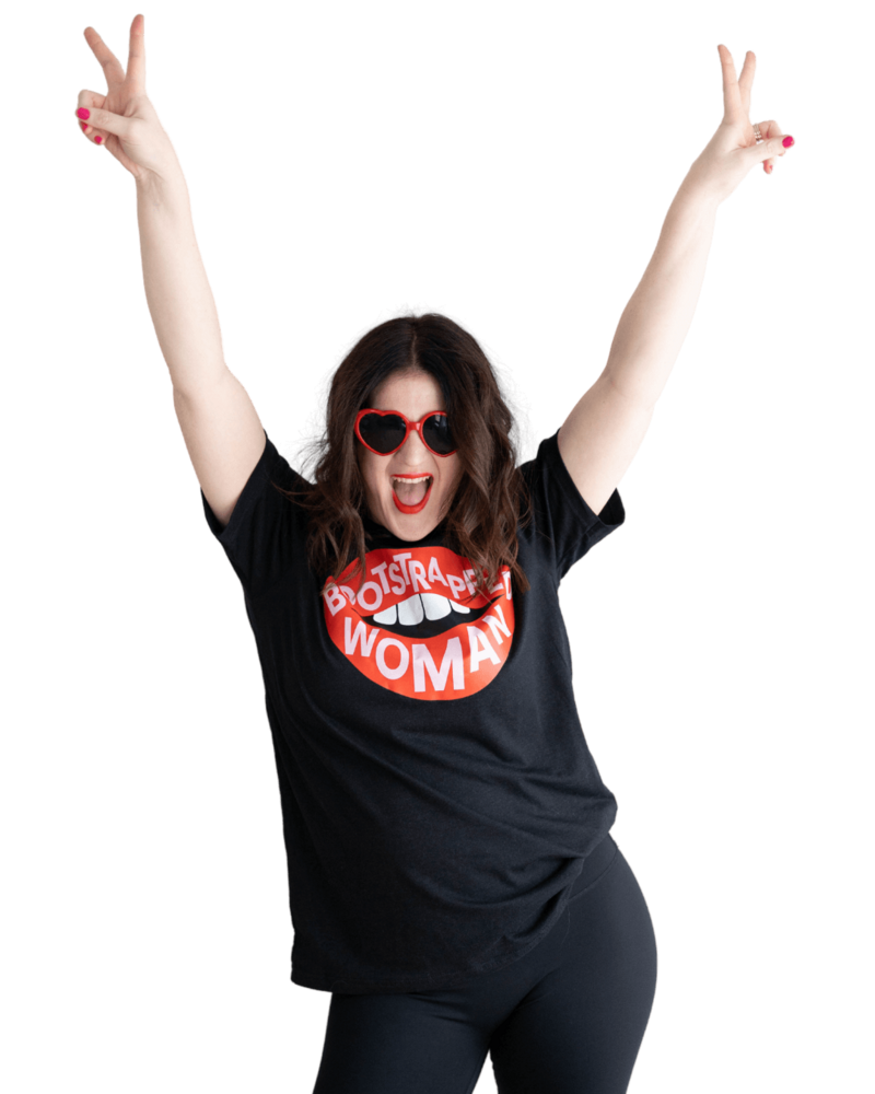 Emily, wearing red sunglasses and a "bootstrapped woman" shirt, does peace signs in the air with her hands.