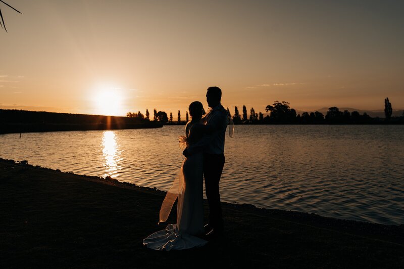 bride and groom at sunset beside a lake at their christchurch wedding